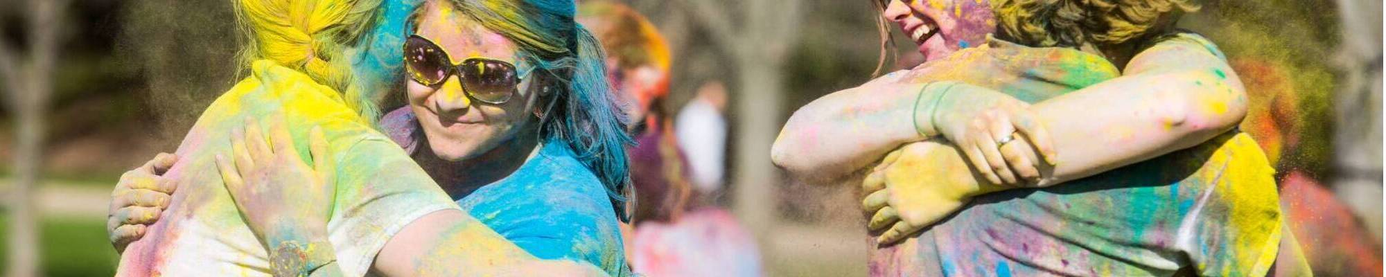 Students covered in colored powder and hugging each other during a Holi festival on campus